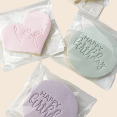 Three cookies with 'Happy Birthday' and 'Love You' text in clear biscuit packaging on a light background