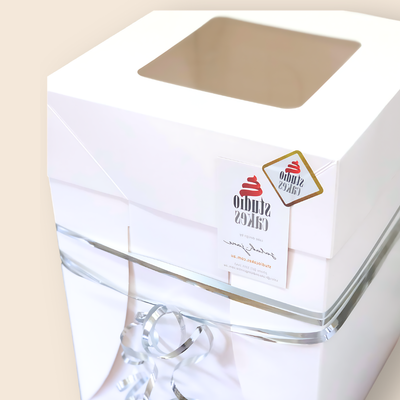 Clear topped cake box assembled to hold a cake securely, finished with a Studio Cakes sticker and ribbon to demonstrate possible assembly of the cake boxes. This is a tall cake box, and other cake box sizes are available.